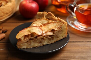 Slice of delicious apple pie served with tea on wooden table, closeup