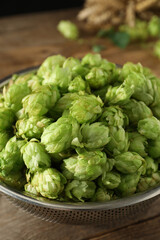 Fresh green hops in sieve on wooden table, closeup