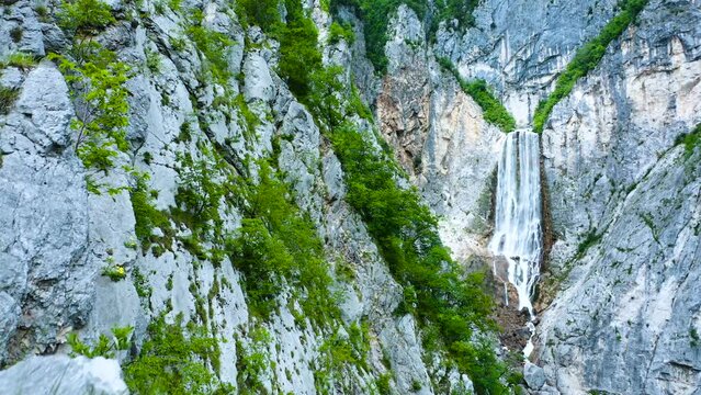 Majestic, Magnificent, Highest Waterfall In Slovenia, Boka Waterfall in The Background Located in The Middle of Cliffs, Canyons, With Trees Hanging From The Cliffs. Rocks And Stones in The Foreground.
