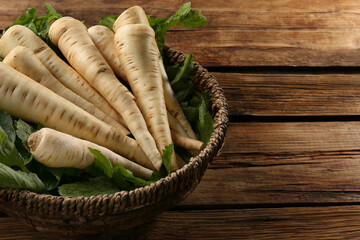 Fresh ripe parsnips in wicker basket on wooden table. Space for text