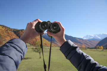 Boy holding binoculars in beautiful mountains on sunny day, closeup