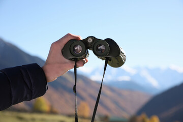 Boy holding binoculars in beautiful mountains on sunny day, closeup