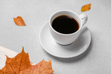 Cup of hot drink, book and autumn leaves on light grey textured table
