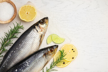 Delicious salted herrings, rosemary, salt and lemon on white wooden table, flat lay. Space for text