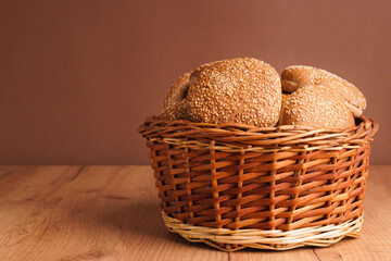 Wicker basket of fresh buns with sesame seeds on wooden table. Space for text