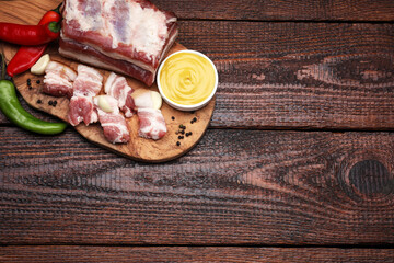 Pieces of pork fatback with chilli pepper and sauce on wooden table, top view. Space for text