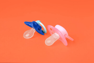 Colorful baby pacifiers on bright orange background