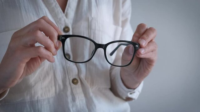 Female wiping eye glasses indoor. A view of woman hands hold her eyeglasses and wiping her lens in the room.