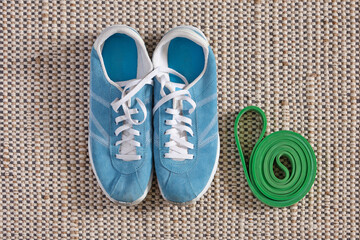 Green fitness band and bright blue natural looking sneakers, with slightly dirty socks from sports, on natural jute and cotton carpet. Sports, home workouts