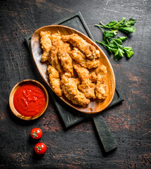 Chicken strips on a cutting Board with parsley and tomato sauce in a bowl.