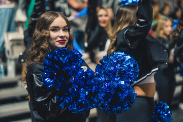 Medium shot of a smilig cheerleader looking at the camera while holding blue pom-poms. Sport...