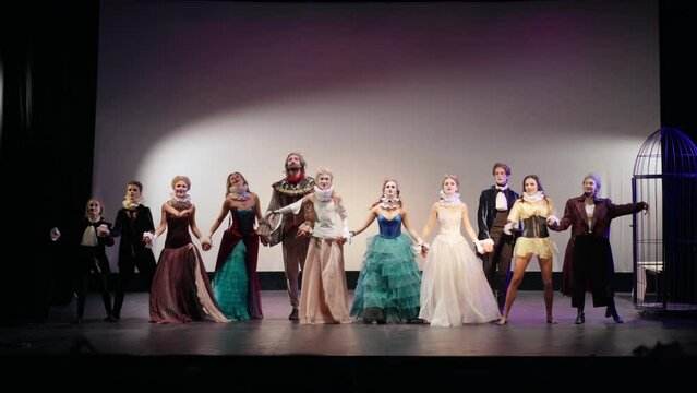 Wide shot theater director holding hands walking with actors and actresses on stage bowing turning walking back. Successful troupe thanking audience smiling