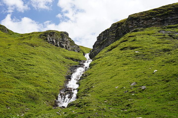Obraz premium waterfall with green gras, blue, cloudy sky in summer in the mountains of austria