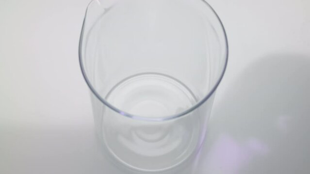 Abstract cosmetics ingredients formulating concept | Macro crane shot of lavender oil is being poured into empty beaker on grey background