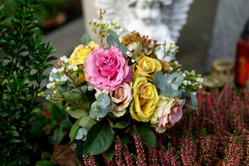 faded pastel roses on a grave in front of an angel in blurry background