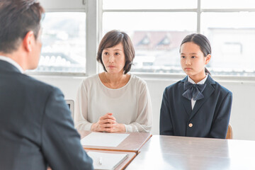 学校の教室で男性教師と三者面談・個人面談する親子（制服の中学生・高校生）