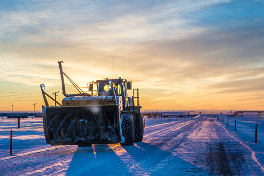 Snowblower at field against dramatic sky during sunset