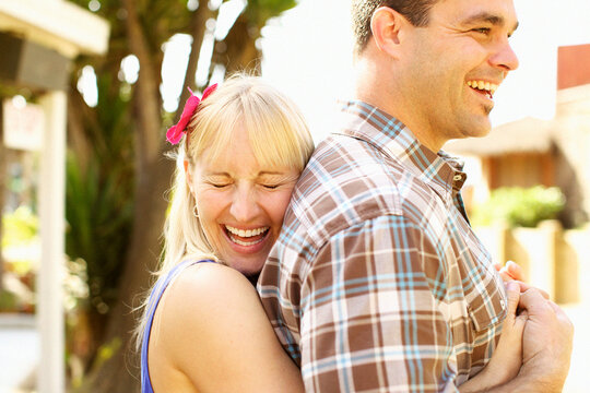 Happy female hugs her fiancee from behind and laughs.
