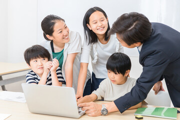 学校の授業でパソコンを使って勉強する小学生の子供達と先生（ICT教育・学校・塾・クラスメイト）