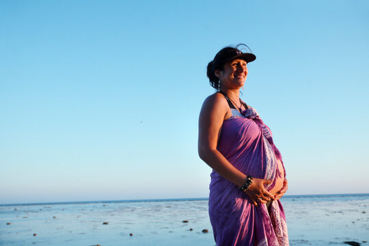 A pregnant woman holds her belly while walking on the beach at sunset on Lady Elliot Island, Australia.