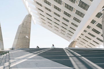 Unrecognizable person riding bicycle under solar panel