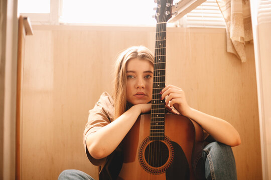 Young woman leaning on guitar while sitting on floor in balcony