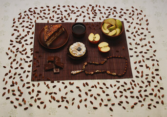 A sweet still life of cakes, milk chocolate, a cup of tea, an apple, an amber pendant, and beech seeds.