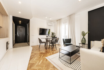 Loft with glass round black dining table with vase and open plan kitchen in contemporary design, wall mounted tv and balcony with sheers