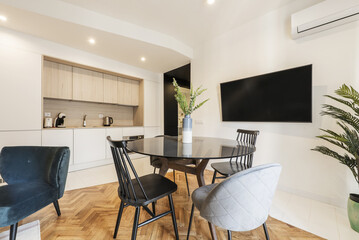 Loft with glass round black dining table with vase and open plan kitchen in contemporary design, wall mounted tv and assorted chairs with varnished oak flooring
