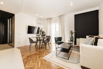 Loft room with round black glass dining table with vase and open plan kitchen in contemporary design, wall mounted tv, fabric sofa and black metal coffee table and balcony with sheers