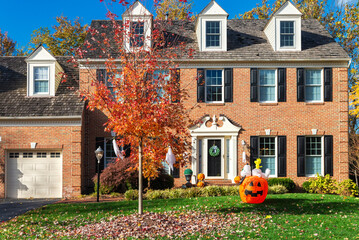 Large Suburban Brick House with Garage and Fall Holiday Decorations. Trimmed lawn and autumn leaves on green grass.