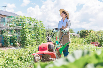 畑を小型トラクターで耕す農家のアジア人女性（農業・田舎暮らし）