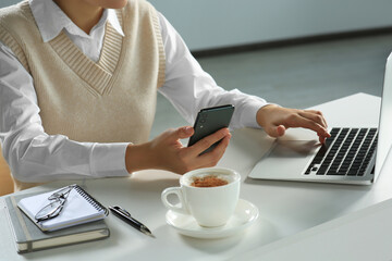 Woman using smartphone at table indoors, closeup