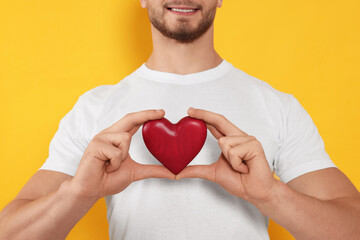 Happy volunteer holding red heart with hands on orange background, closeup