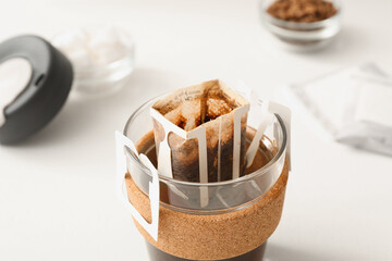 Glass cup with drip coffee bag on white table, closeup