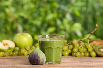 Glass of fresh green smoothie and ingredients on wooden table outdoors, space for text