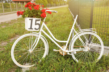 Fototapeta na wymiar White bicycle with red flowers in basket on street
