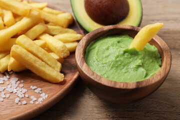 Plate with french fries, guacamole dip and avocado served on wooden table, closeup