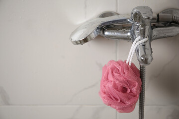 Pink shower puff hanging on faucet in bathroom, space for text