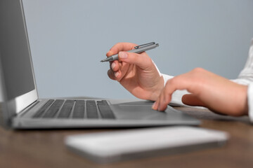 Woman with smartphone and pen working on laptop at wooden table, closeup. Electronic document management