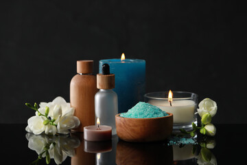 Beautiful spa composition with different care products, burning candles and flowers on black mirror surface