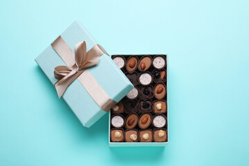 Open box of delicious chocolate candies on light blue background, flat lay