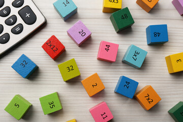 Colorful cubes with numbers and multiplications near calculator on white wooden table, flat lay