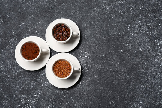 Cups with different types of coffee on dark grey table, flat lay. Space for text