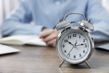 White alarm clock and man working at table, closeup. Space for text