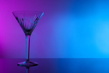 Empty clean martini glass on mirror table in neon lights, space for text