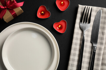 Beautiful table setting with burning candles and decorative hearts on black table for romantic dinner, flat lay