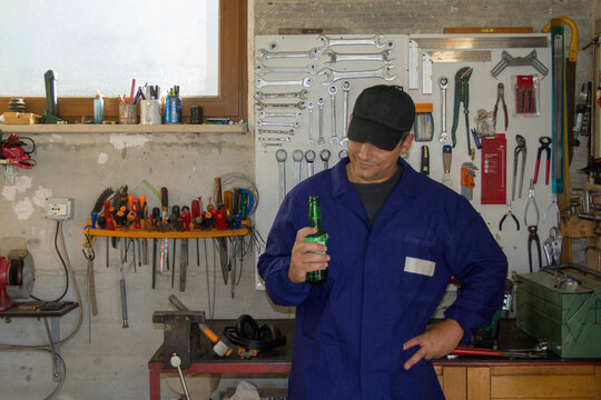 Image of a man in overalls holding a bottle of beer in his workshop. Break, relax after work.

