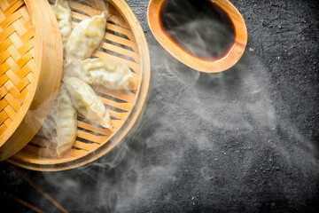 Hot Chinese traditional gedza dumplings in bamboo steamer with soy sauce. - obrazy, fototapety, plakaty
