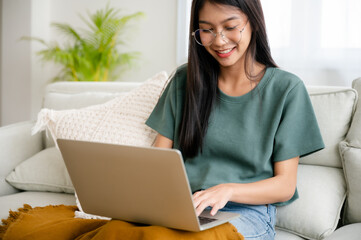 Smiling young asian woman working on laptop at home. Attractive asia female using computer remote...